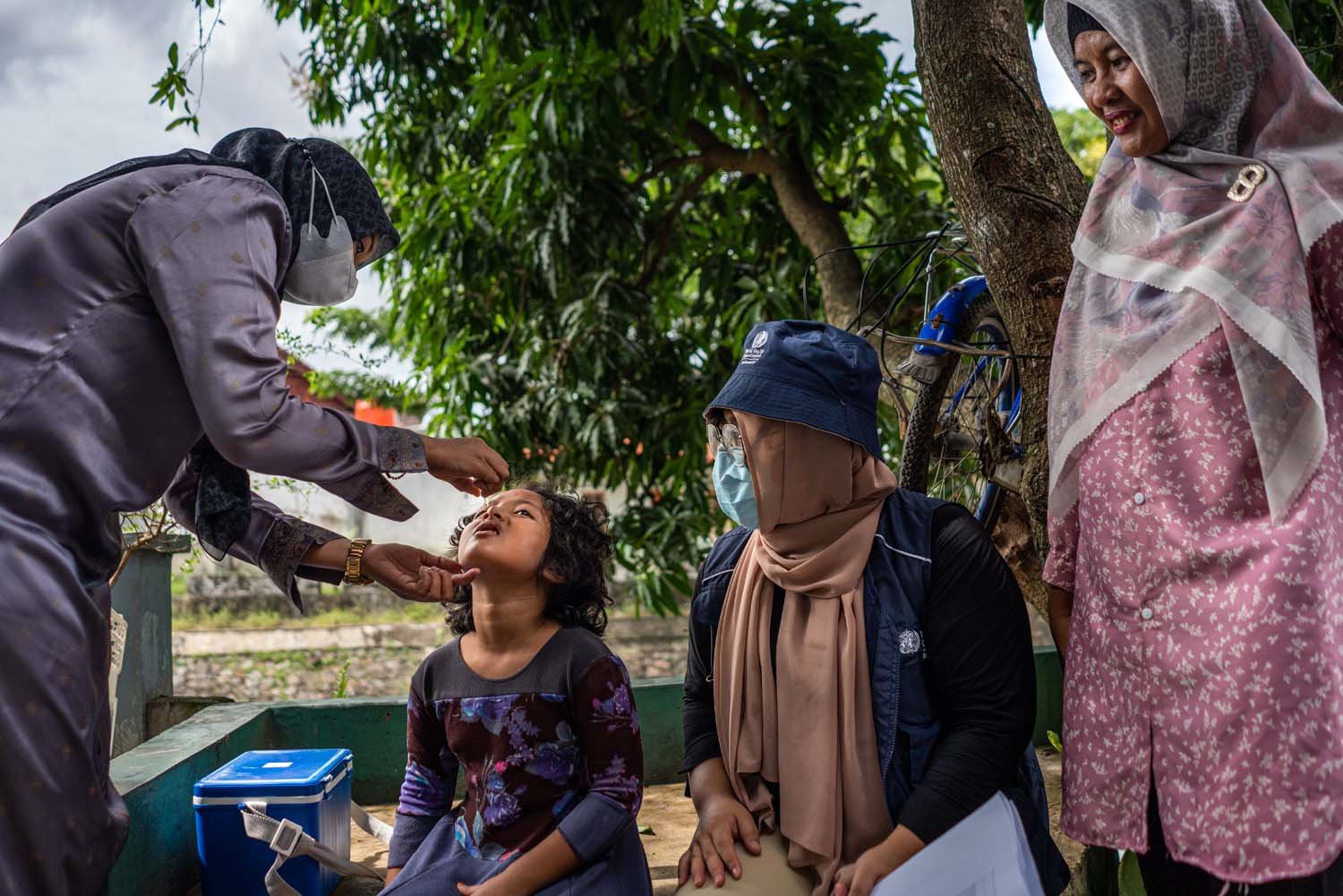 A doctor vaccinated a girl, while two officers from Puskesmas and WHO watched the scene.