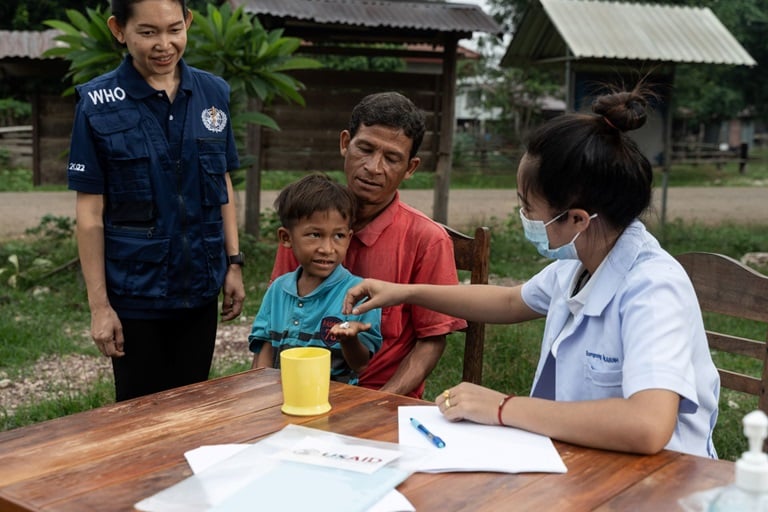 A boy sits on his father's lap while receiving medications in Lao PDR